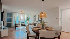 A modern living room with a dining area, featuring a round table, chairs, a hanging light fixture, and a large window with curtains. - SaLarena - Life at the beach (Medianía Alta)