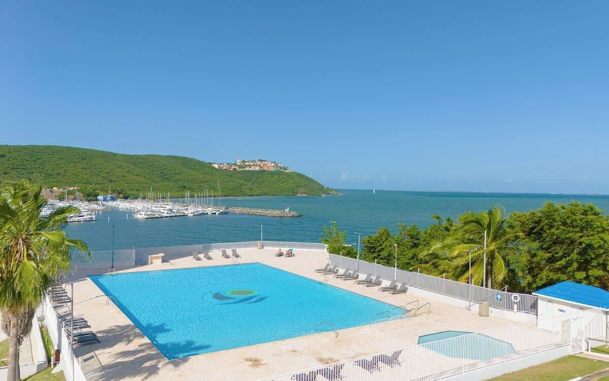 A swimming pool with a view of the sea and a hill with buildings.