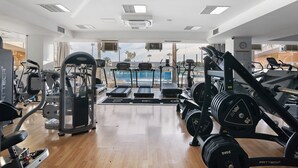 A gym with cardio machines, weightlifting equipment, and a view of a pool. - Apartment 'Paraíso do Atlântico' with Shared Pool, Garden, and Wi-Fi (Albufeira)