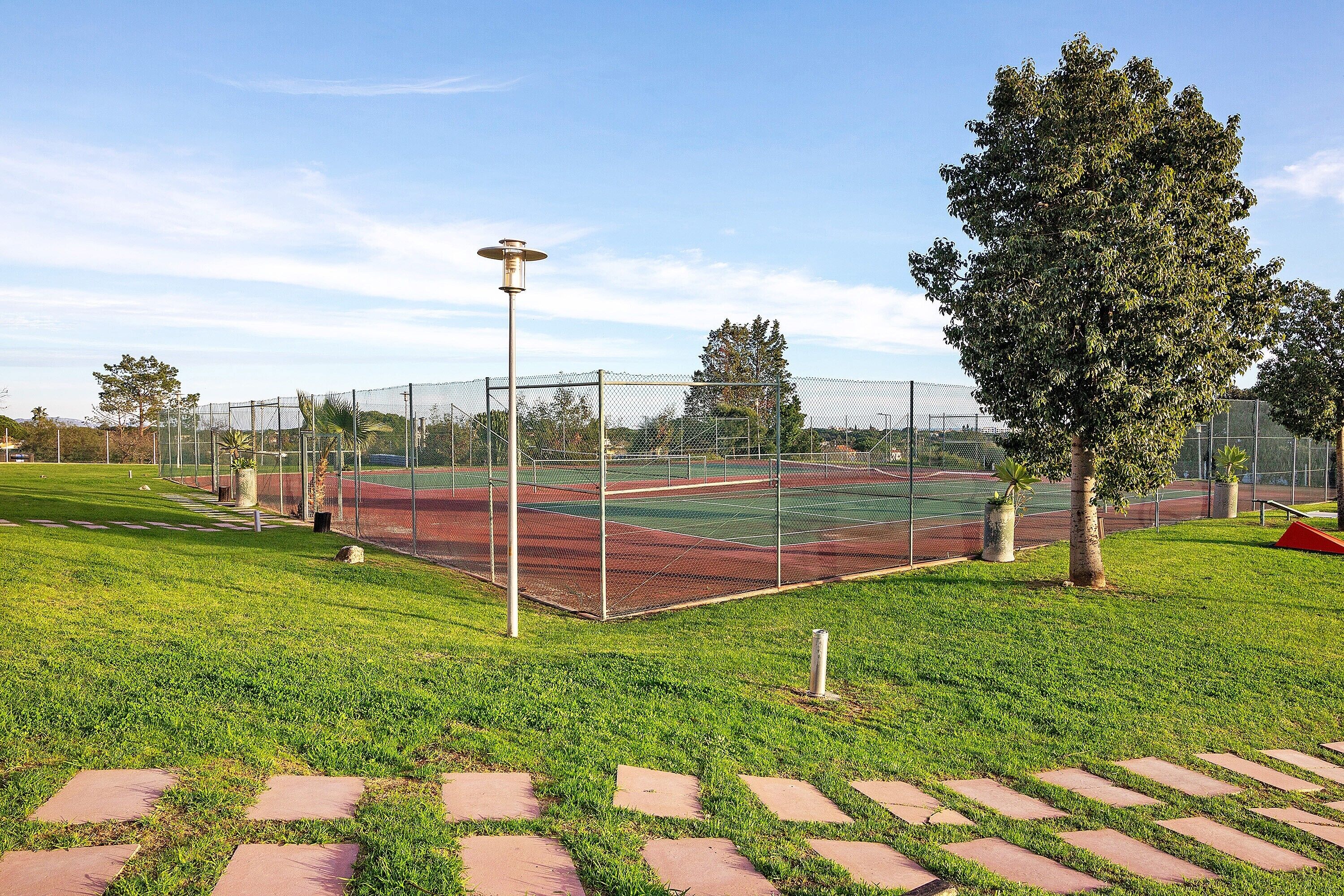 Een tennisbaan met hekwerk, bomen en een heldere lucht.