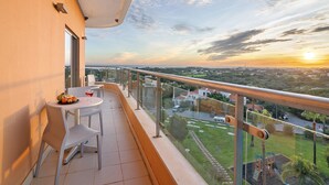 A balcony with a table, chairs, and a view of the cityscape during sunset. - Apartment 'Paraíso do Atlântico' with Shared Pool, Garden, and Wi-Fi (Albufeira)