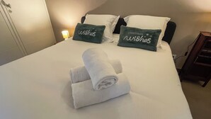 Een net opgemaakt bed met witte lakens en twee groene kussens met de tekst 'Christmas Wishes'.