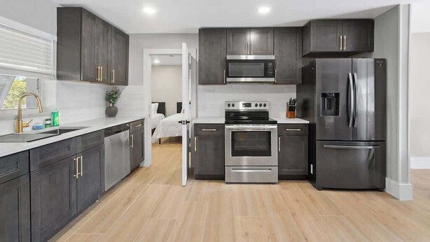 Une cuisine moderne avec des meubles de couleur sombre, des appareils électroménagers en acier inoxydable et un plancher en bois.