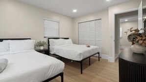 Une chambre avec deux lits, une table de chevet ornée d’une plante, et une porte donnant sur une autre pièce.