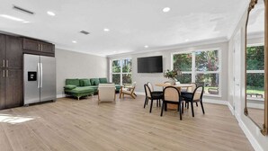 Un vaste espace de vie comprenant une cuisine moderne, une table à manger avec des chaises et une grande fenêtre donnant sur l’extérieur.