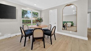 Un espace repas comprenant une table ronde et des chaises, un grand miroir et une vue sur un espace extérieur verdoyant.