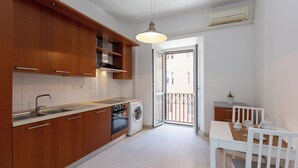 A modern kitchen with wooden cabinets, a built-in oven, a washing machine, and a dining area with a table and chairs. - Rental in Rome Cesare Apartment (Rome)