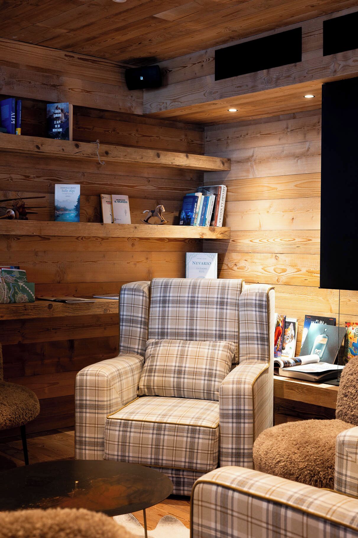 A cozy cabin interior with plaid-patterned seating, a wooden bookshelf, and a flat-screen TV.