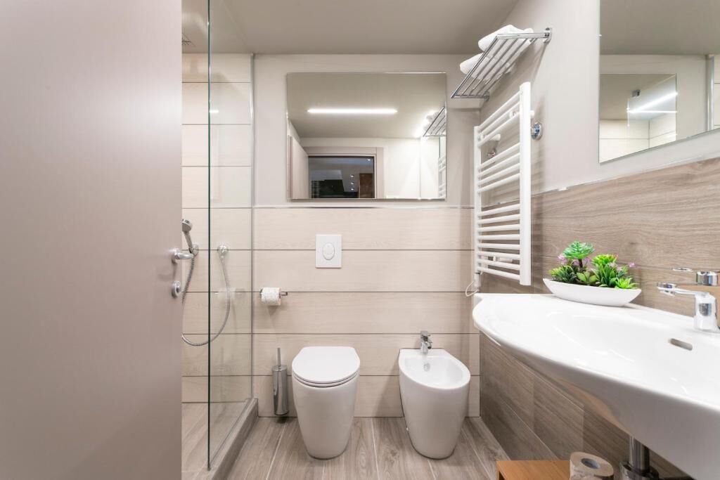 Ein modernes Badezimmer mit Duschkabine aus Glas, Toilette, Bidet, Waschbecken mit Spiegel und einer kleinen Pflanze auf der Ablagefläche.
