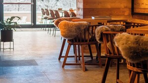A restaurant interior with wooden walls, a large window with a view of snow-covered trees, and several tables with chairs. - Le Mallet, Courmayeur, Alpine Homesuite (Courmayeur)