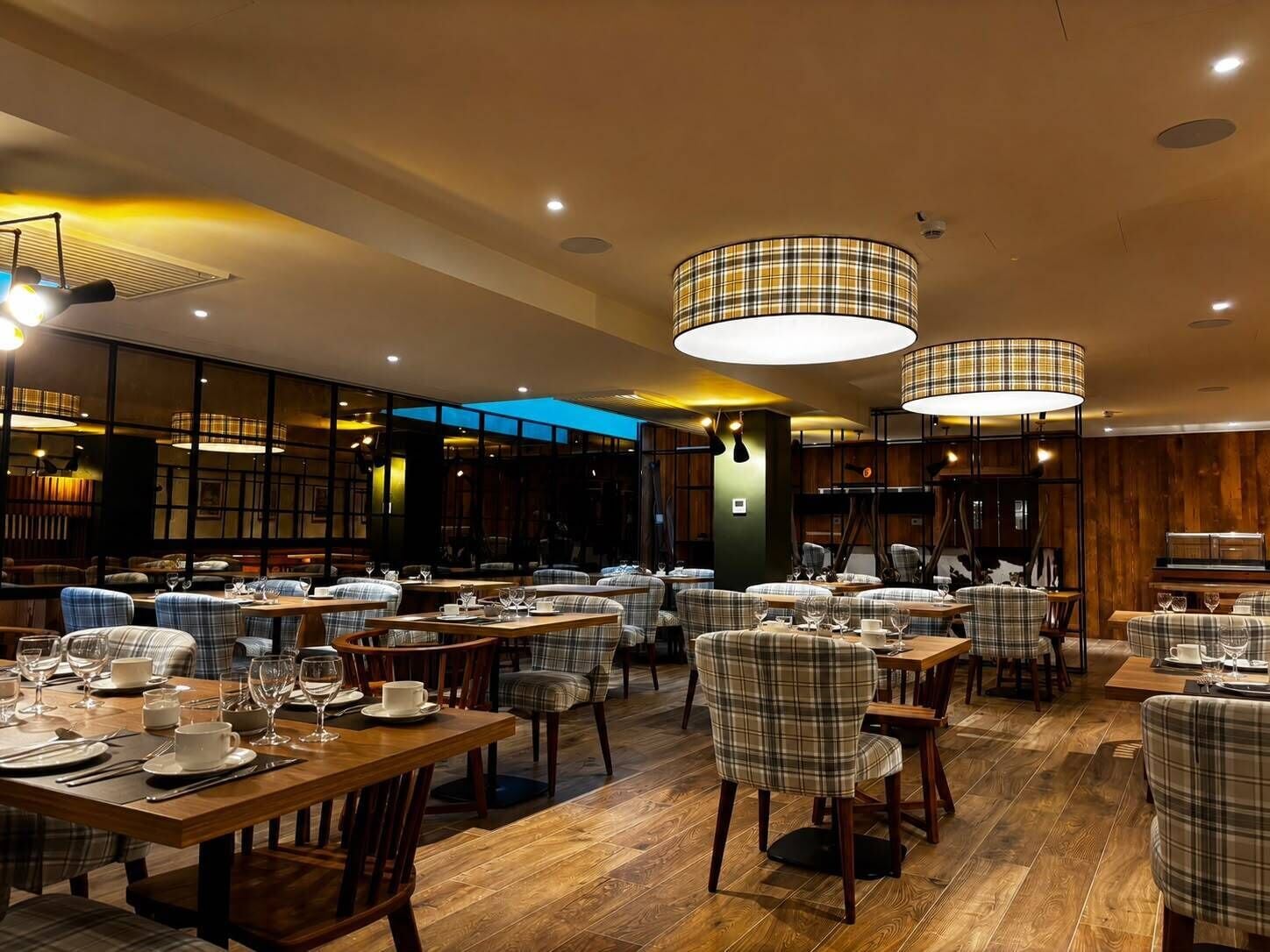 Un restaurante con varias mesas y sillas, suelo de madera e iluminación colgante.