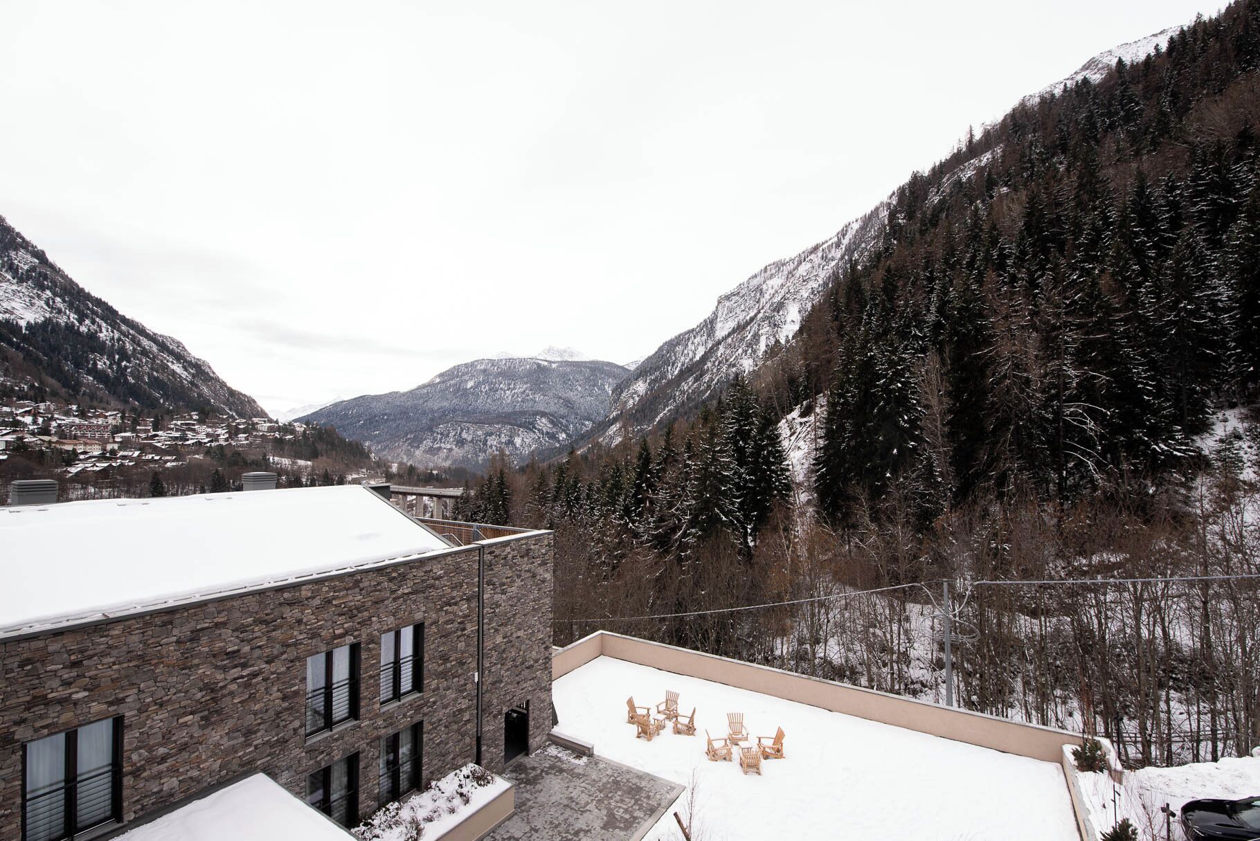 A building with a stone facade and a flat roof, surrounded by snow-covered mountains and trees.