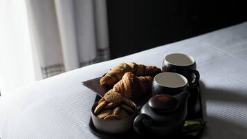A neatly arranged breakfast setting on a bed with croissants, cookies, and two black cups, likely containing coffee or tea.