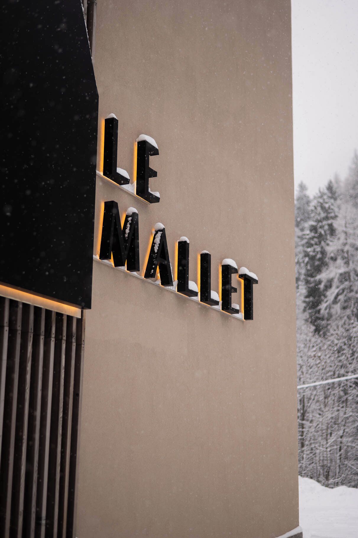 A building with the sign "LE MALLET" illuminated in black letters against a beige wall.