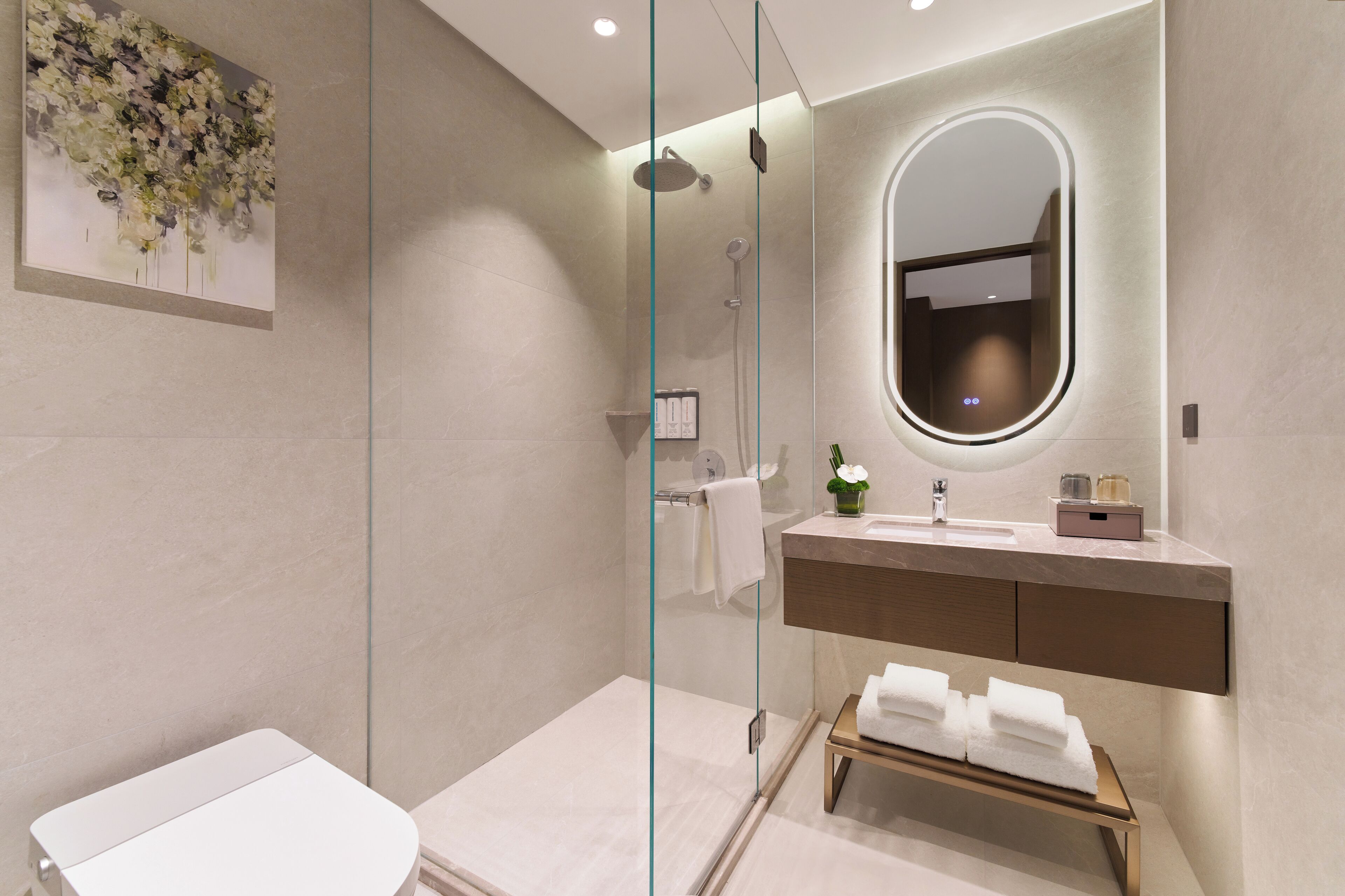 A modern bathroom with a glass-enclosed shower, a vanity with a mirror, and a bench with towels.