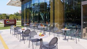 An outdoor seating area with tables and chairs, a sign for Hyatt Place, and a glass building reflecting the surroundings.