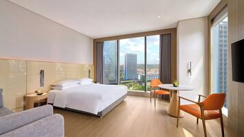 Habitación de hotel moderna con cama, escritorio y silla, un amplio ventanal con vista a la ciudad y un televisor de pantalla plana.