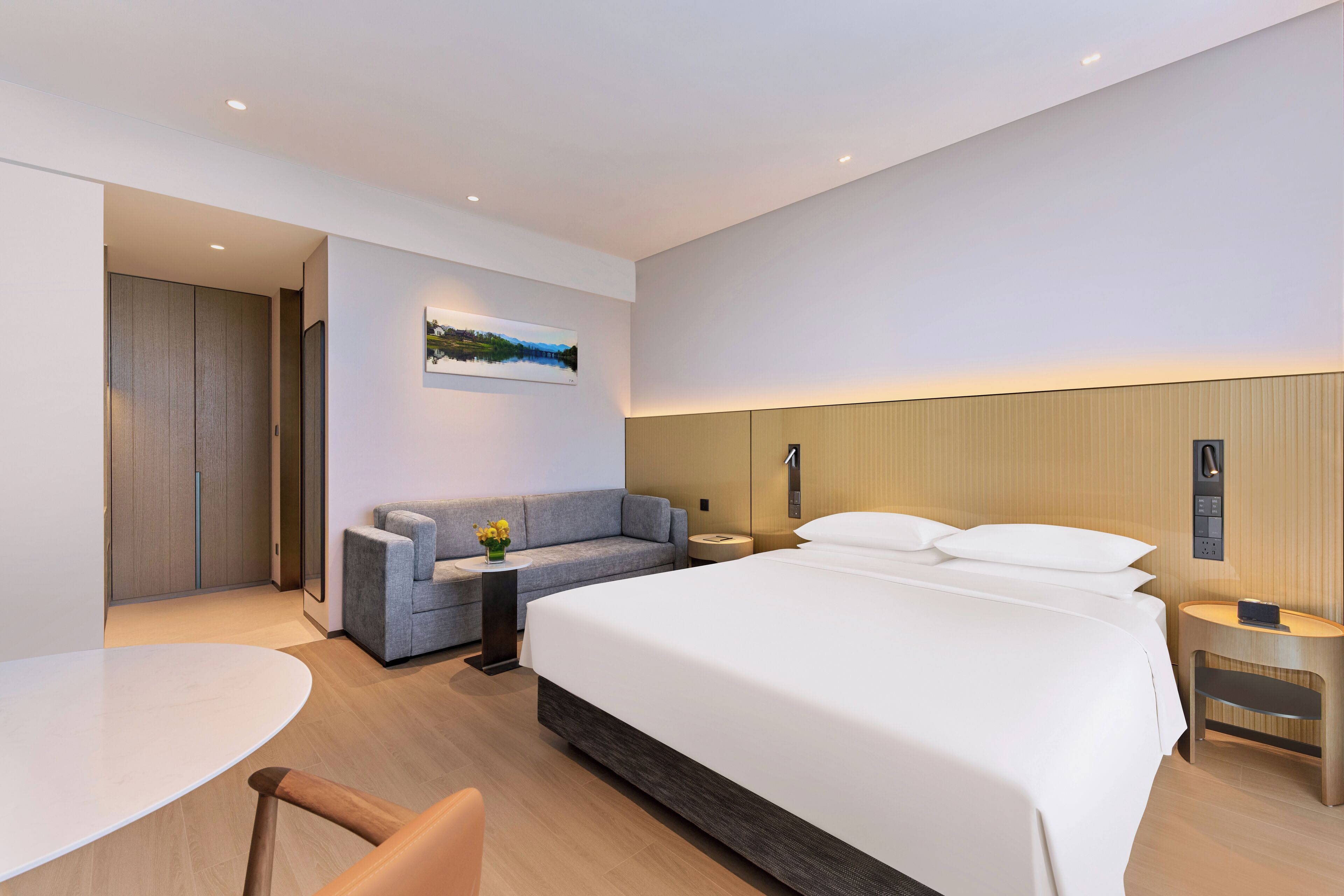 Una habitación de hotel moderna con una cama grande, un sofá, una mesita y un televisor montado en la pared.