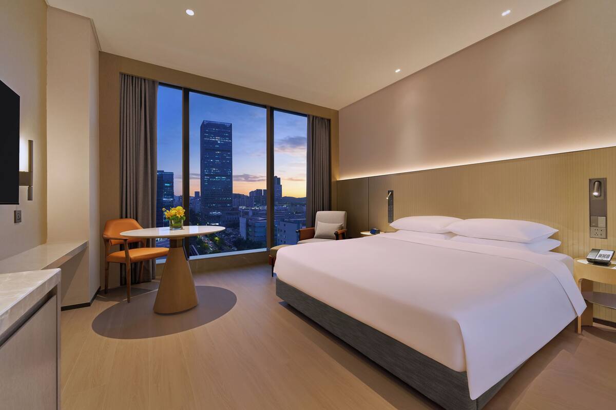 Een moderne hotelkamer met een groot bed, een bureau en uitzicht op de skyline van de stad.
