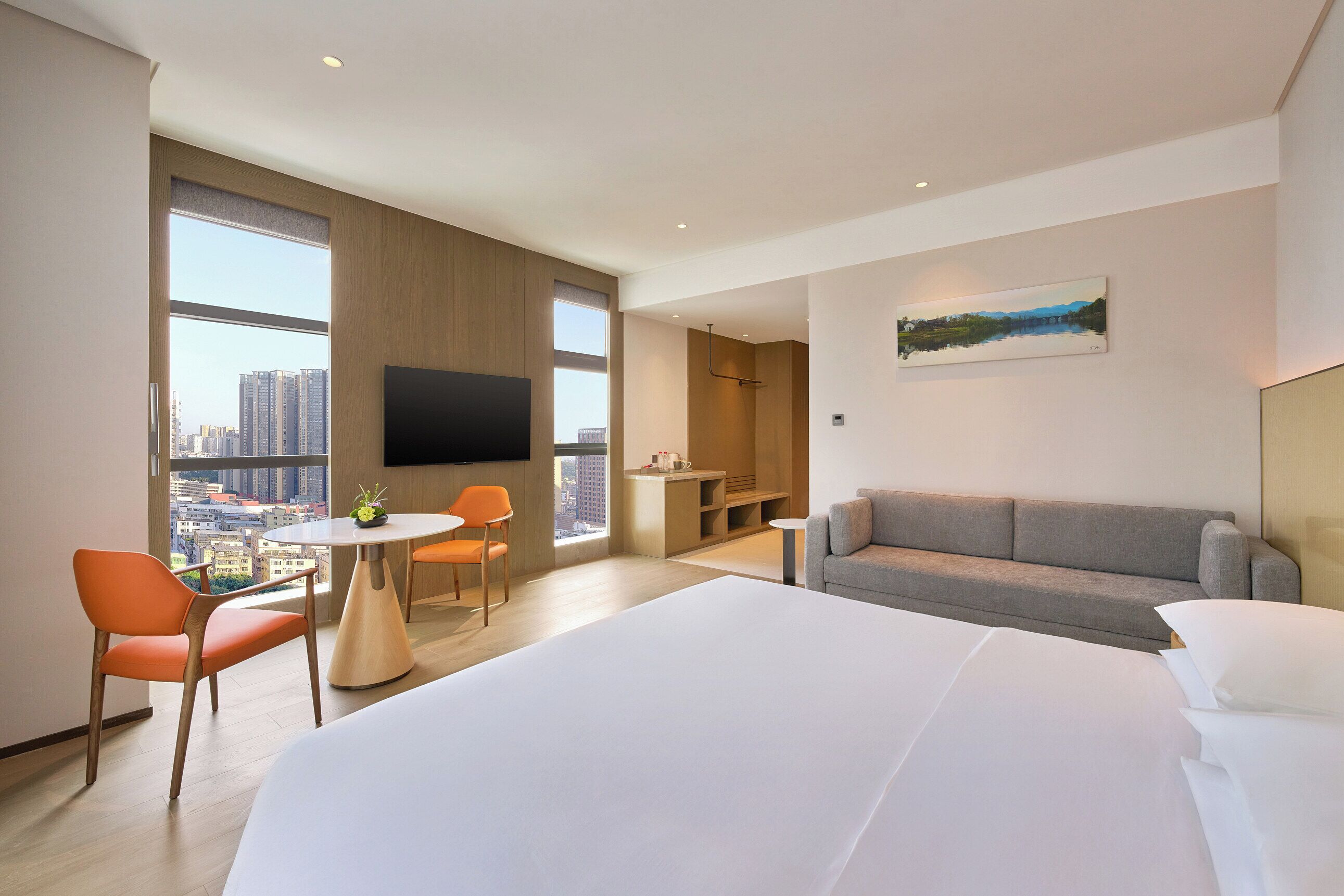 Habitación de hotel moderna con una cama grande, un sofá, una mesa de comedor con sillas, un televisor y vistas a la ciudad.