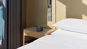 A hotel room with a bed, a bedside table with a clock, a power outlet, and a wall-mounted control panel.
