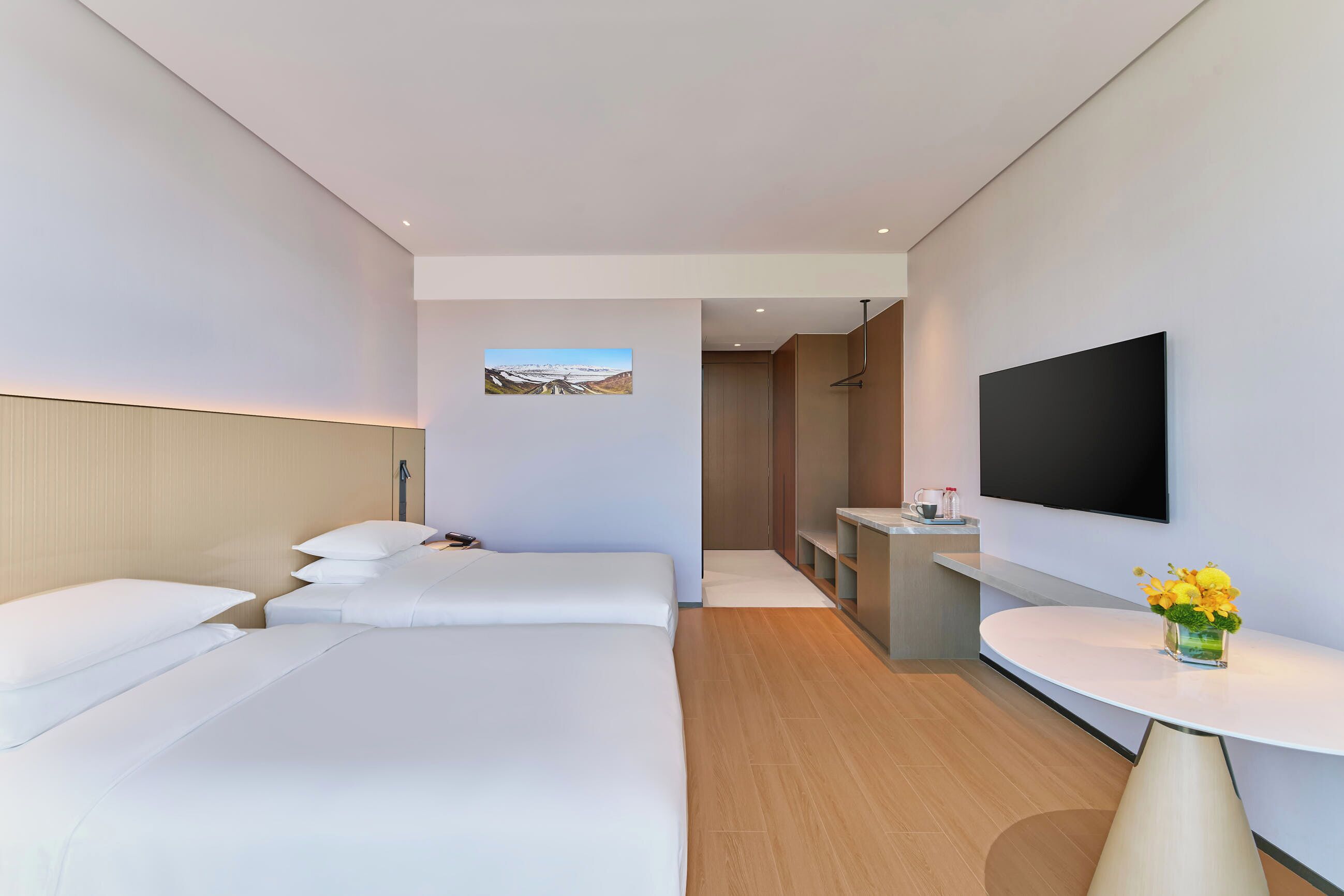 Una habitación de hotel moderna con dos camas, un televisor, una mesita con un florero y vistas a las montañas a través de una ventana.
