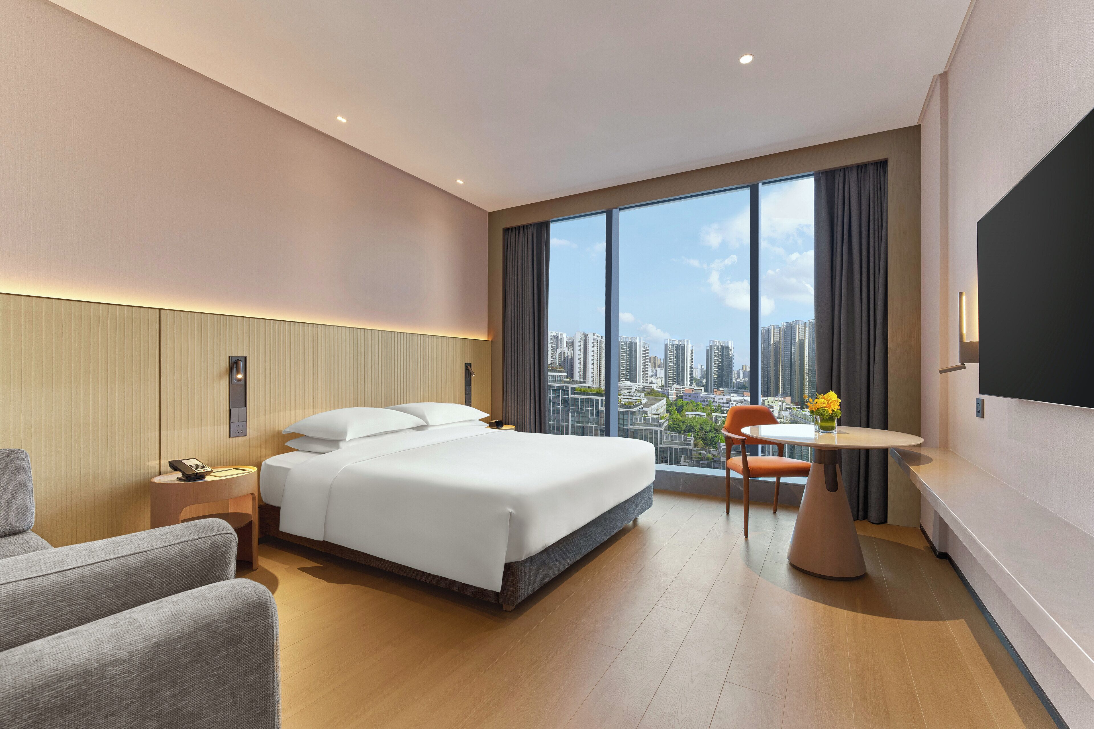 Una habitación de hotel moderna con una cama grande, un escritorio, una silla y vistas a la ciudad.
