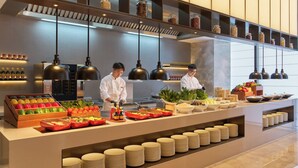 A modern kitchen with chefs preparing food, a buffet with various dishes, and neatly stacked plates. - Hyatt Place Shenzhen Longgang (Shenzhen)