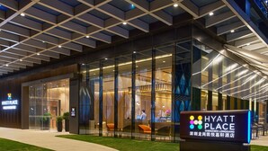 A Hyatt Place hotel exterior with a modern glass facade, a well-lit entrance, and a landscaped area with a pathway leading to the entrance. - Hyatt Place Shenzhen Longgang (Shenzhen)