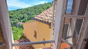 Une fenêtre donnant sur une colline, un bâtiment avec un toit en tuiles et un balcon.