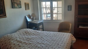 Une chambre à coucher avec un lit, un bureau avec une lampe, une chaise et une fenêtre avec des volets.