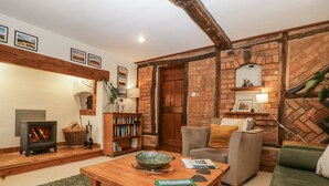 A cozy living room with a fireplace, a bookshelf, a sofa, and a coffee table. - Magpie Cottage (Worcester)