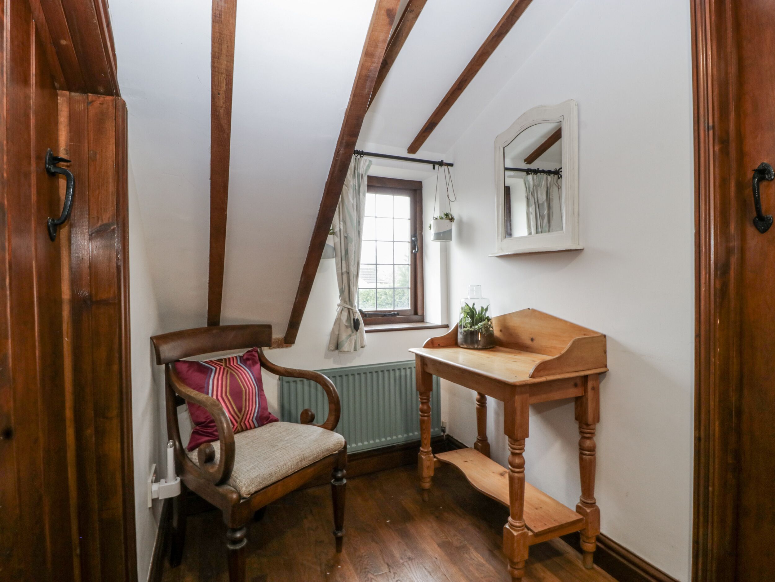 Una habitación con una silla y una mesa de madera, una ventana con cortina y un radiador.