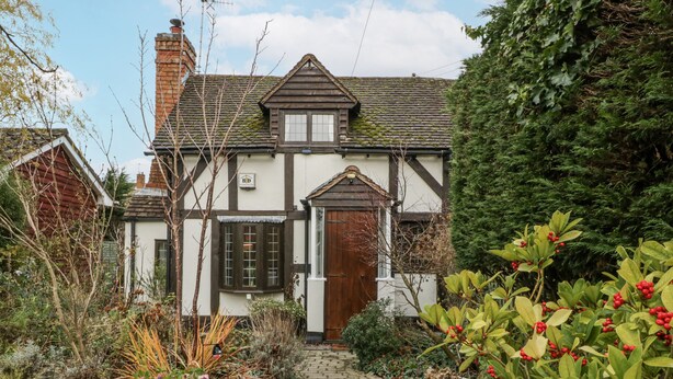 A traditional house with a brick chimney, a wooden door, and a garden with various plants and a pathway leading to the entrance. - Magpie Cottage (Worcester)