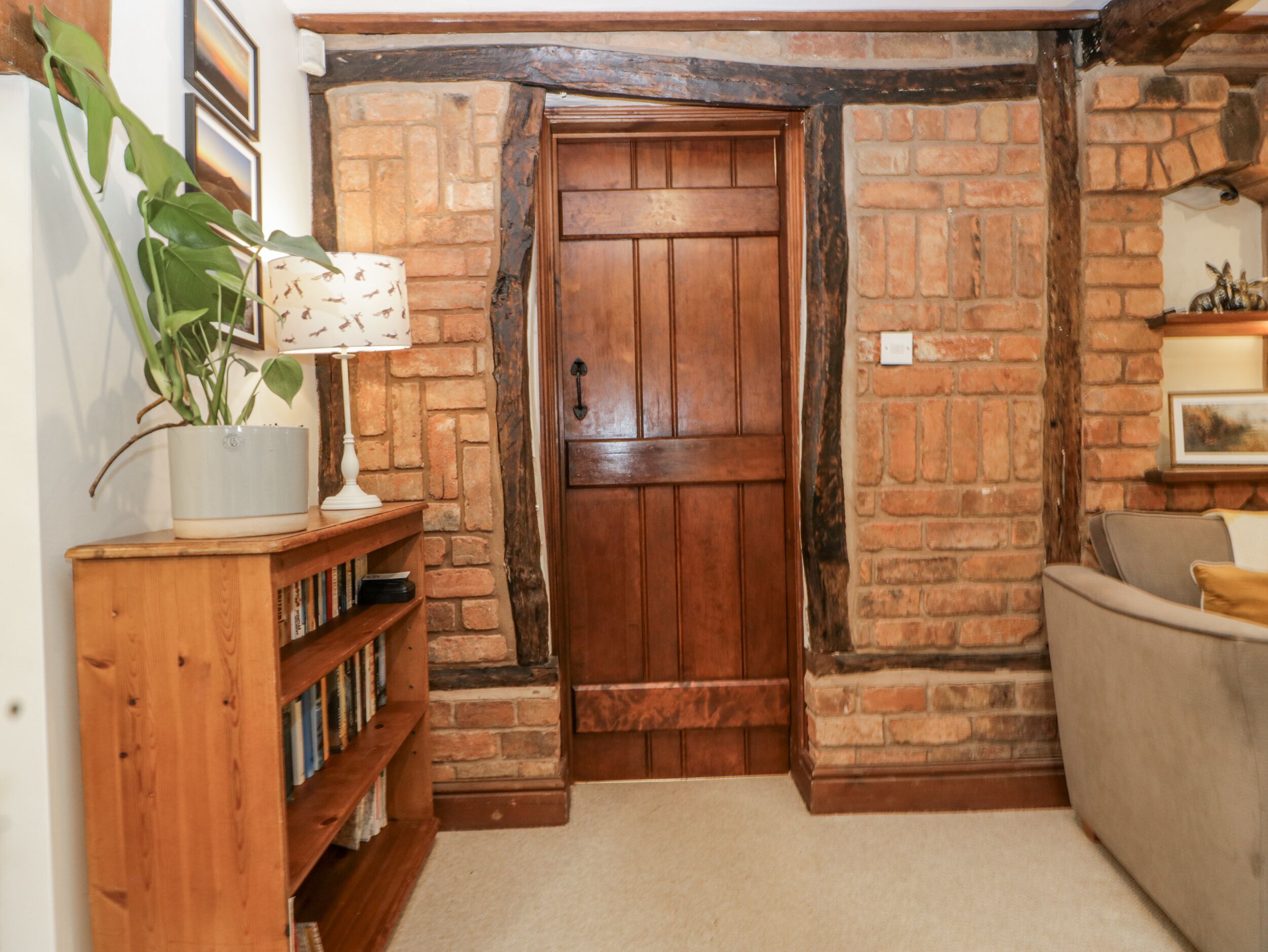 A cozy room with a wooden door, a bookshelf, a potted plant, and a brick wall.