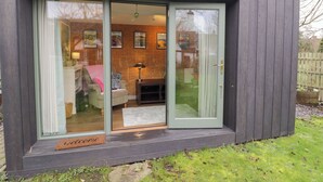 A modern house with a glass door leading to a living room with a fireplace, a sofa, and a lamp. - Magpie Cottage (Worcester)