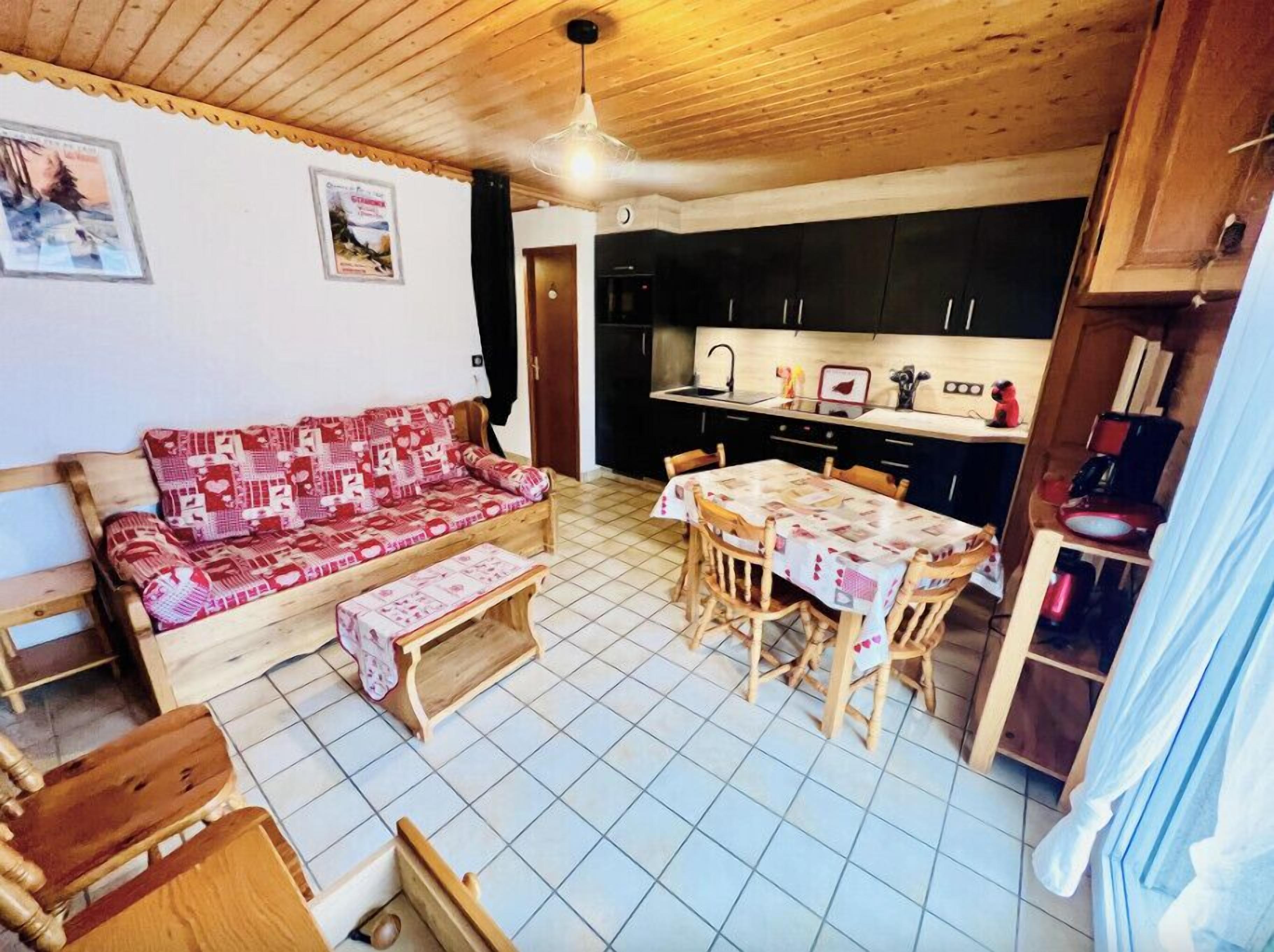 Una sala de estar acogedora con un sofá de madera y una mesa de comedor, una cocina con armarios negros y un ventilador de techo.