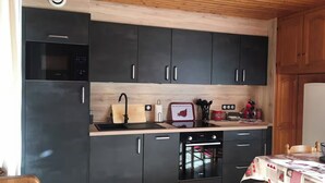 Una cocina moderna con armarios oscuros, techo de madera, horno empotrado y zona de comedor con una mesa cubierta por un mantel estampado.