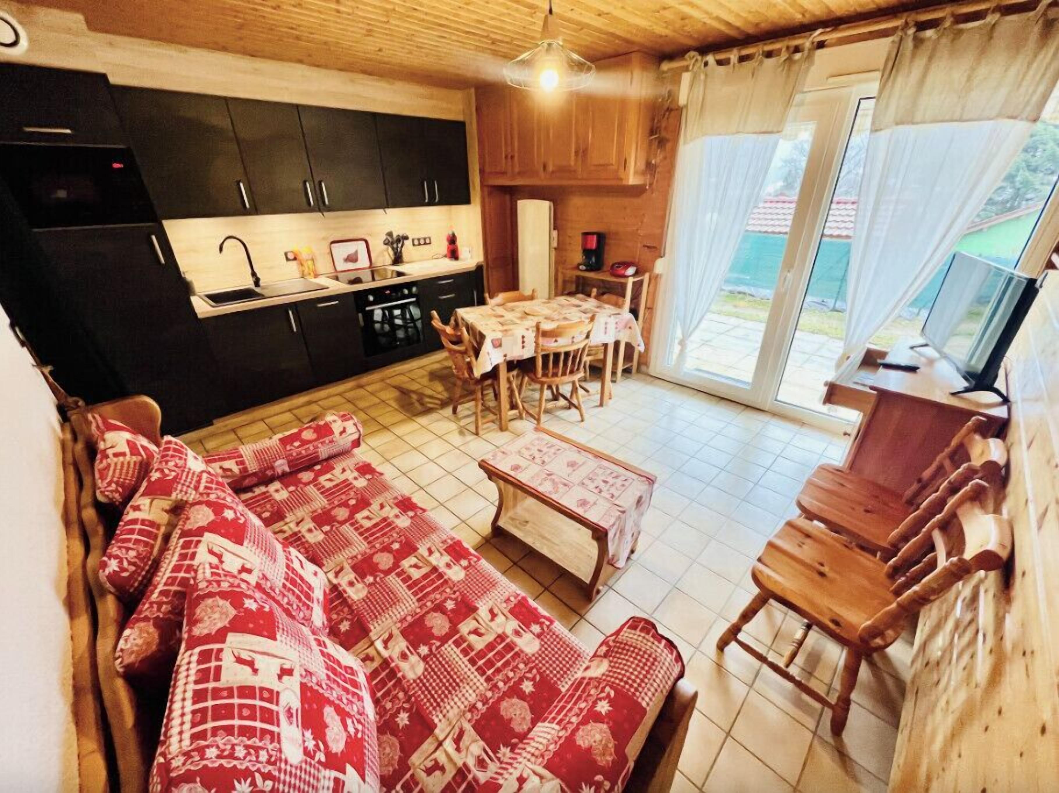 A cozy living room with a sofa set, a dining table, and chairs. There is a kitchen area with cabinets and a sink.