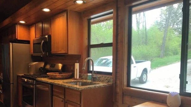 Cocina con armarios de madera, encimera de granito y vista a un camión de carga blanco estacionado afuera.