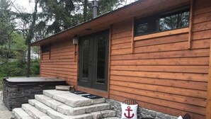 Una cabaña de madera con escalones de piedra que conducen a una puerta, un jacuzzi y zona de estar al aire libre.