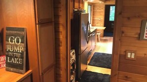 Interior de una cabaña de madera con zona de cocina, un refrigerador y un letrero que dice 'GO JUMP IN THE LAKE'.