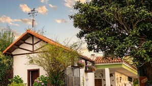 Una casa tradicional con techo de tejas, puerta de madera y jardín con plantas en macetas.