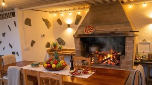 A rustic dining area with a brick fireplace, wooden furniture, and a fruit bowl on the table. - Ursula's Cozy Retreat in Santa Ursula (Santa Ursula)