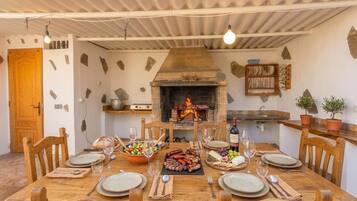 An outdoor dining area with a stone fireplace, wooden table, and chairs.