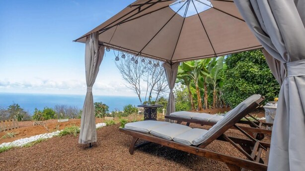 Una silla de lounge de madera bajo un paraguas grande, con vista al océano.