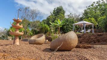 A garden with a decorative fountain, wicker furniture, and a covered seating area.