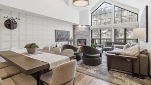 Un vaste espace de vie doté d’un haut plafond, de grandes fenêtres, d’une cheminée et d’un coin repas avec une longue table et des sièges confortables.