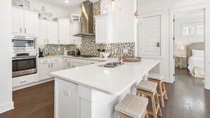A modern kitchen with white cabinetry, a large island, stainless steel appliances, and a patterned backsplash. - Prominence Salt & Light - 6 Seat Golf Cart Included (Walton County)