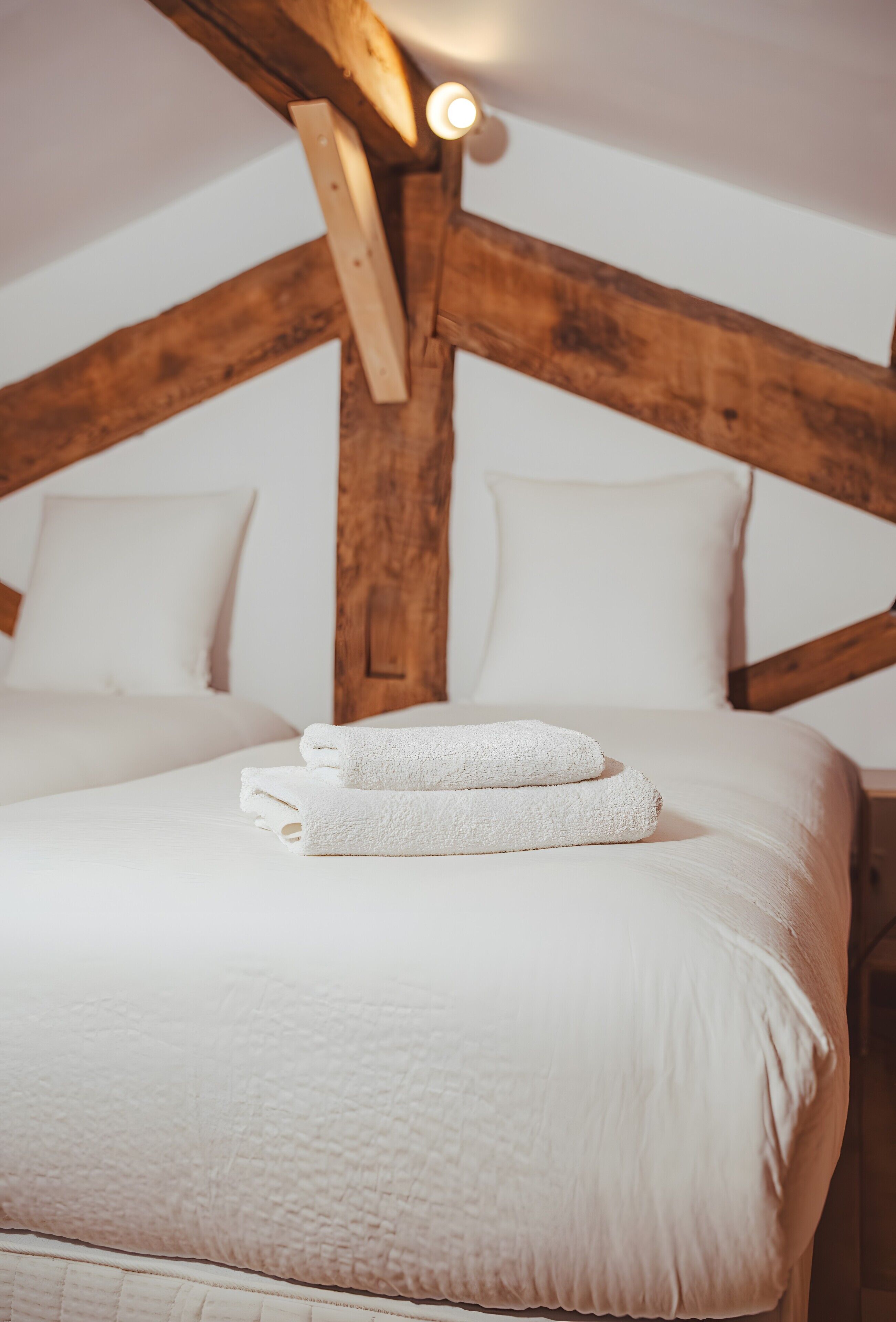 A bed with white linens and towels, wooden beams, and a white pillow.